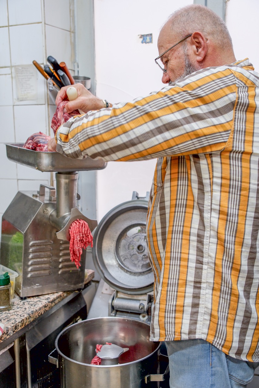 Le chef passant la viande au hachoir pour préparer le kebbé