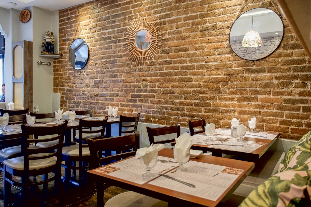 Salle du restaurant Baladna aux murs de briques apparentes, miroirs soleil et tables dressées